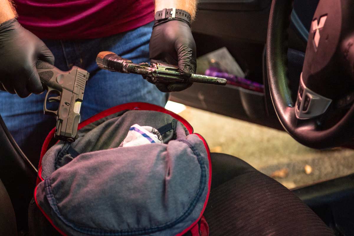 gloved hands take guns out of a bag in a car
