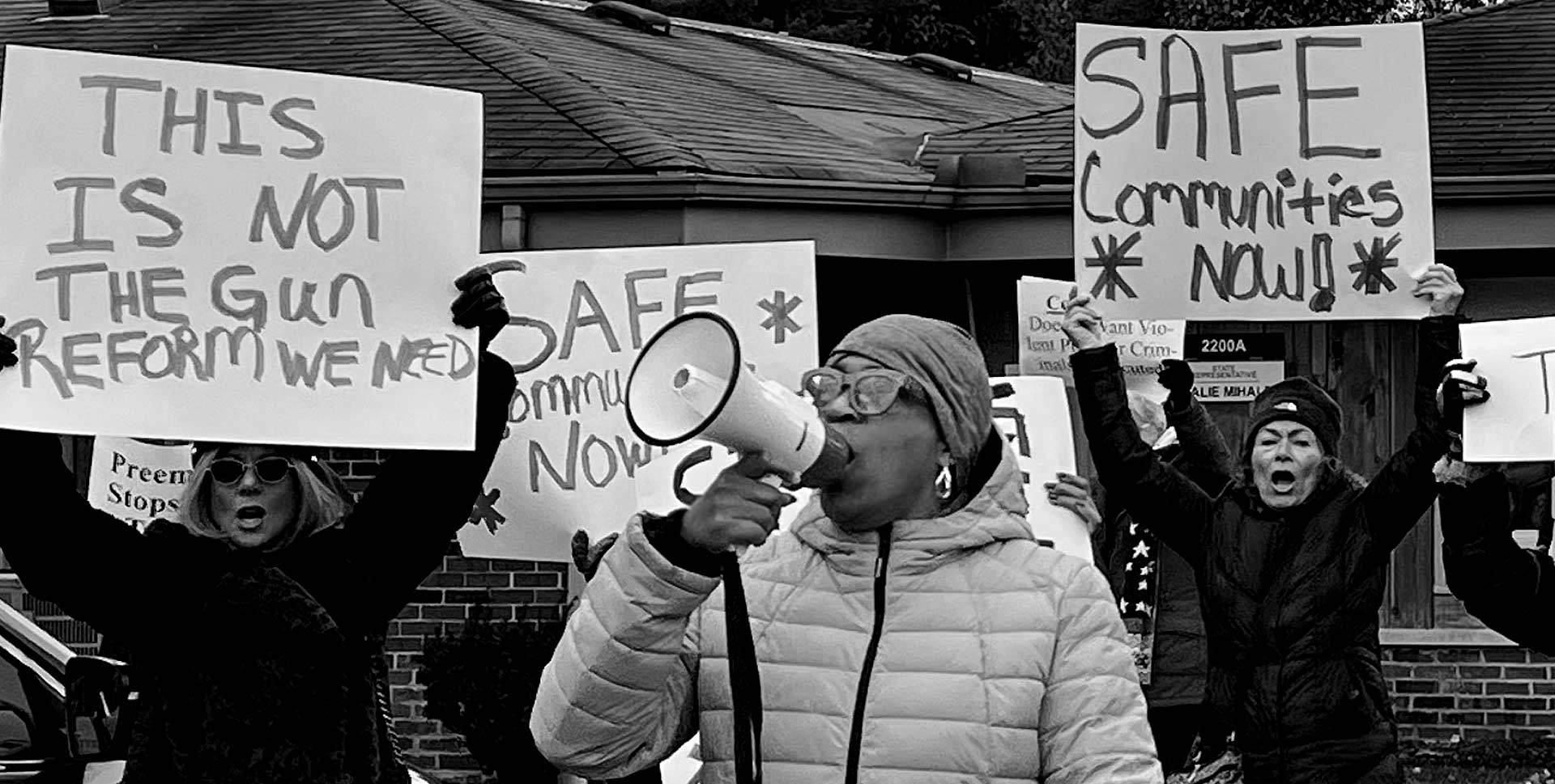 woman speaking with megaphone with supporters behind her carrying signs