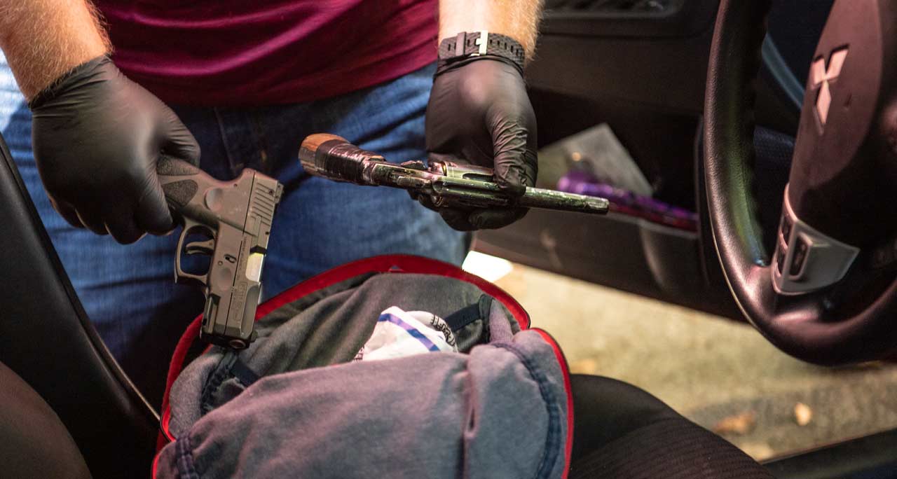 person wearing gloves taking guns out of car